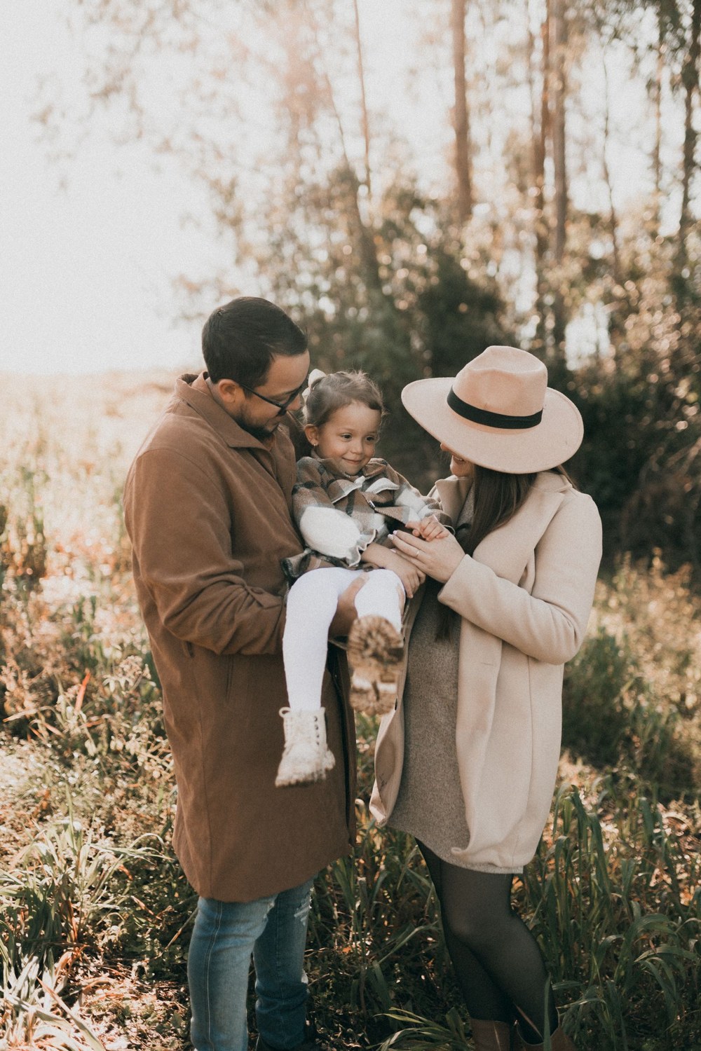 Two parents holding their child in a sunlit woodland
