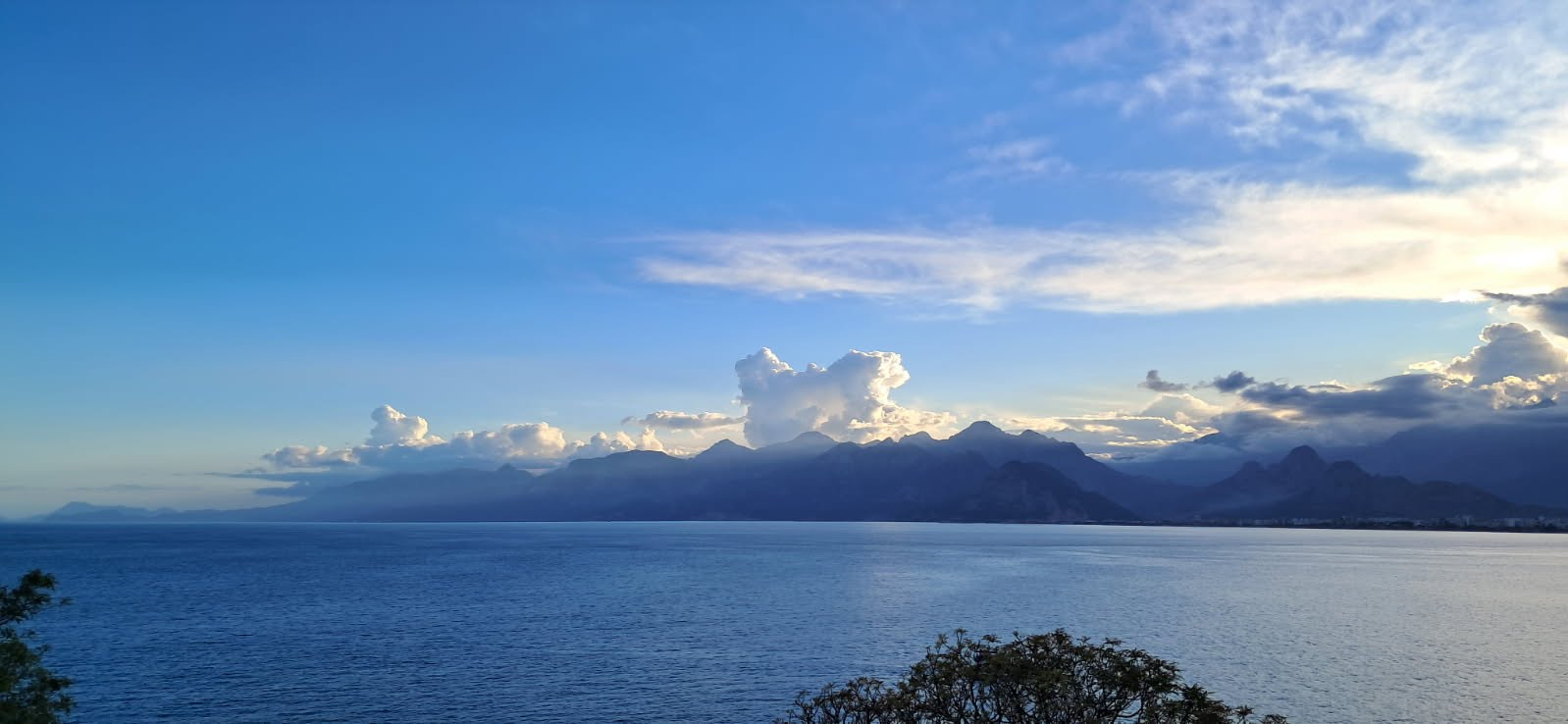 Sunlight above mountains across a calm blue sea